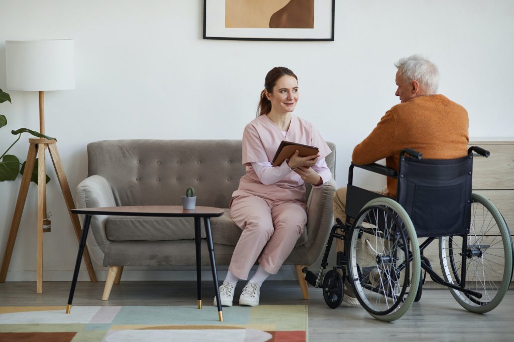 Smiling Female Nurse Surveying Disabled Senior Man